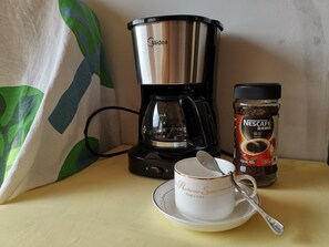 A coffee maker, a jar of Nescafé, and a cup with a spoon on a table.
