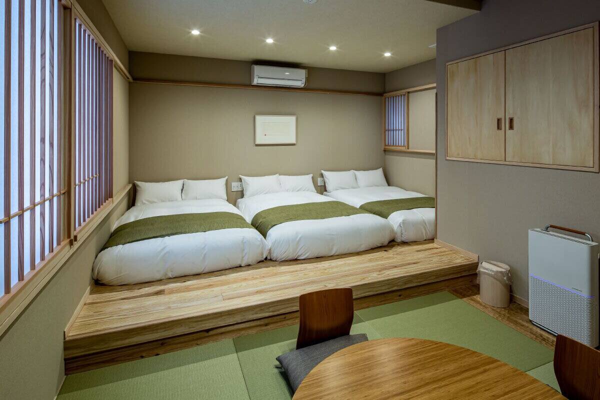 A room with three beds aligned against a wall, a small table, and a radiator.