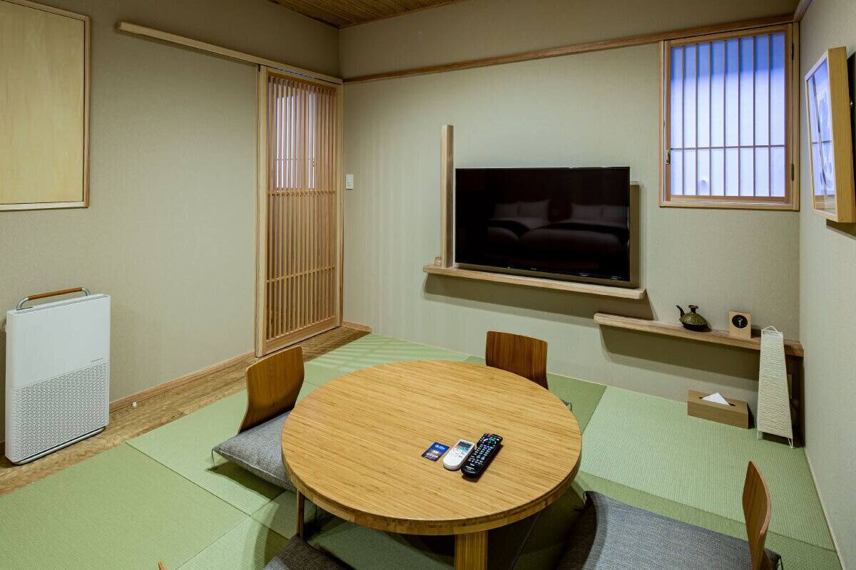 A traditional Japanese-style room with tatami flooring, a tatami mat table, a television mounted on the wall, and a futon bed.