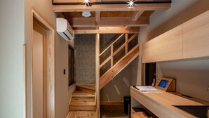 Un pasillo estrecho con una escalera de madera que conduce a una zona superior. Un escritorio con lavamanos está ubicado contra la pared.