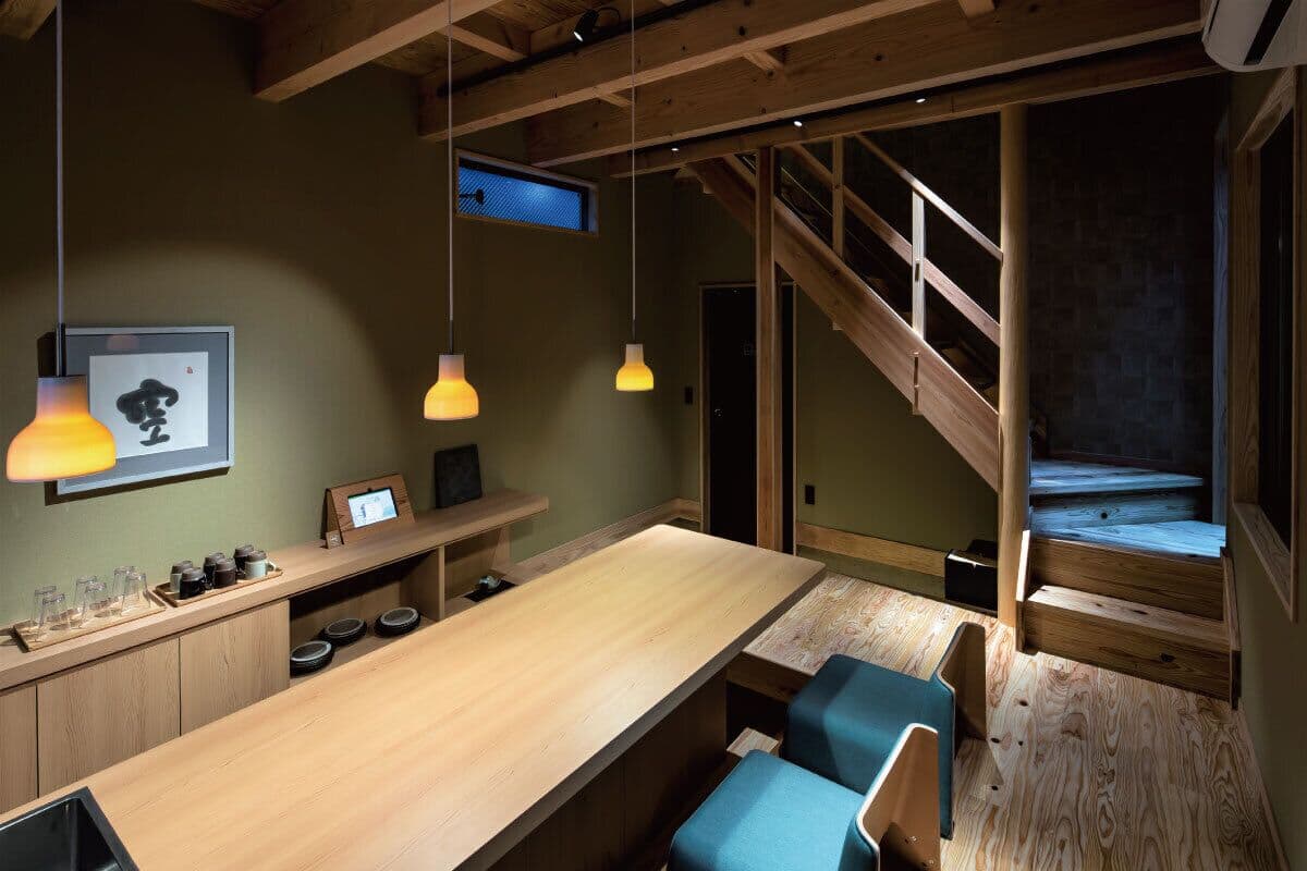 A modern kitchen with a wooden island, pendant lights, and a staircase leading to an upper level.