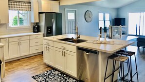 Una cucina moderna con mobili bianchi, frigorifero in acciaio inossidabile, lavastoviglie e un'ampia finestra.