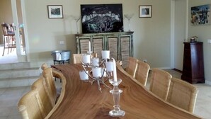 Uma sala de jantar com uma grande mesa de madeira, cadeiras de vime e um armário com quadros emoldurados.