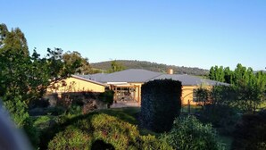 Uma casa moderna com um amplo jardim frontal, um alpendre coberto e vista para uma colina ao fundo.