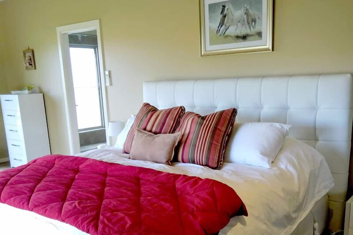 A neatly made bed with a red blanket and striped pillows, a white headboard, and a framed picture on the wall.