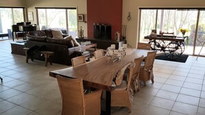 Uma sala de estar espaçosa com uma grande mesa de jantar de madeira, rodeada por cadeiras de vime, um sofá de couro e um piano.