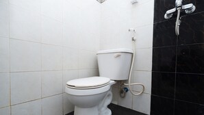 Des toilettes blanches, avec un réservoir et un accessoire de type bidet, dans une salle de bain dont les murs sont recouverts de carreaux noirs et blancs.