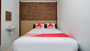 Une chambre d’hôtel avec un lit, une tête de lit en bois, un lavabo blanc et un miroir au mur.