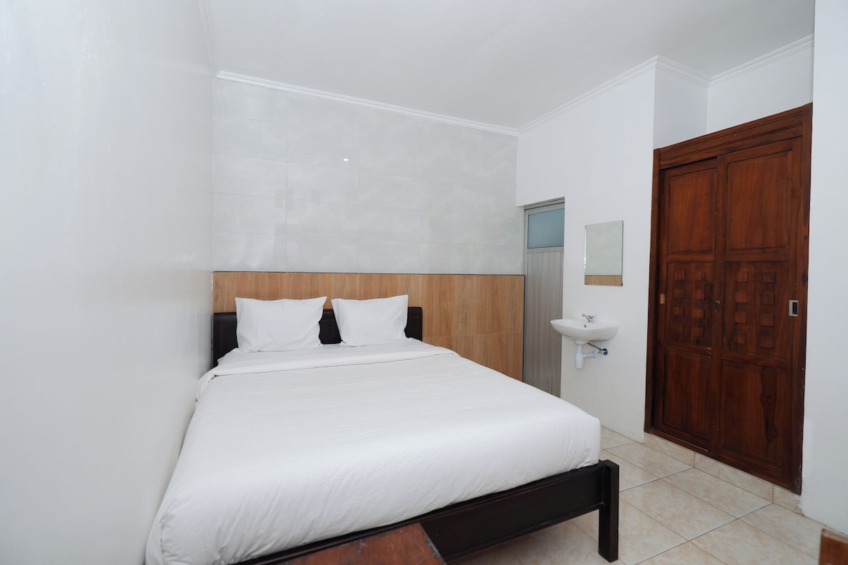 A bedroom with a bed, a wooden headboard, a white wall, a wooden door, and a small sink.