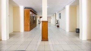 Un pasillo con pisos de baldosas blancas, puertas de madera y columnas.