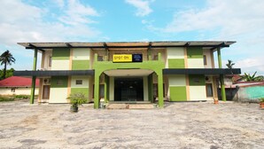 Un hotel con fachada verde y beige, un letrero que dice "SPOT ON HOTEL VIBRANO 2809", y un área de entrada pavimentada con plantas en macetas.