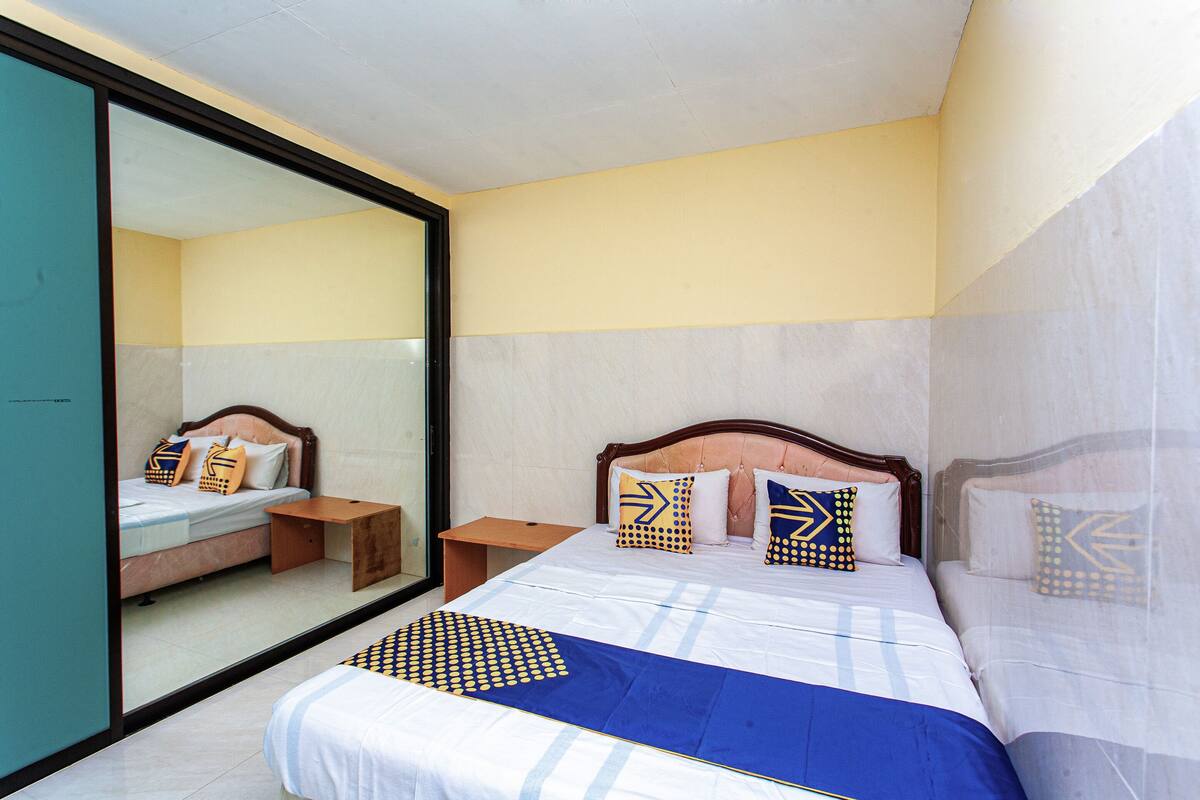 Quarto de hotel com um espelho grande, uma cama com colcha azul e branca, e almofadas a combinar.