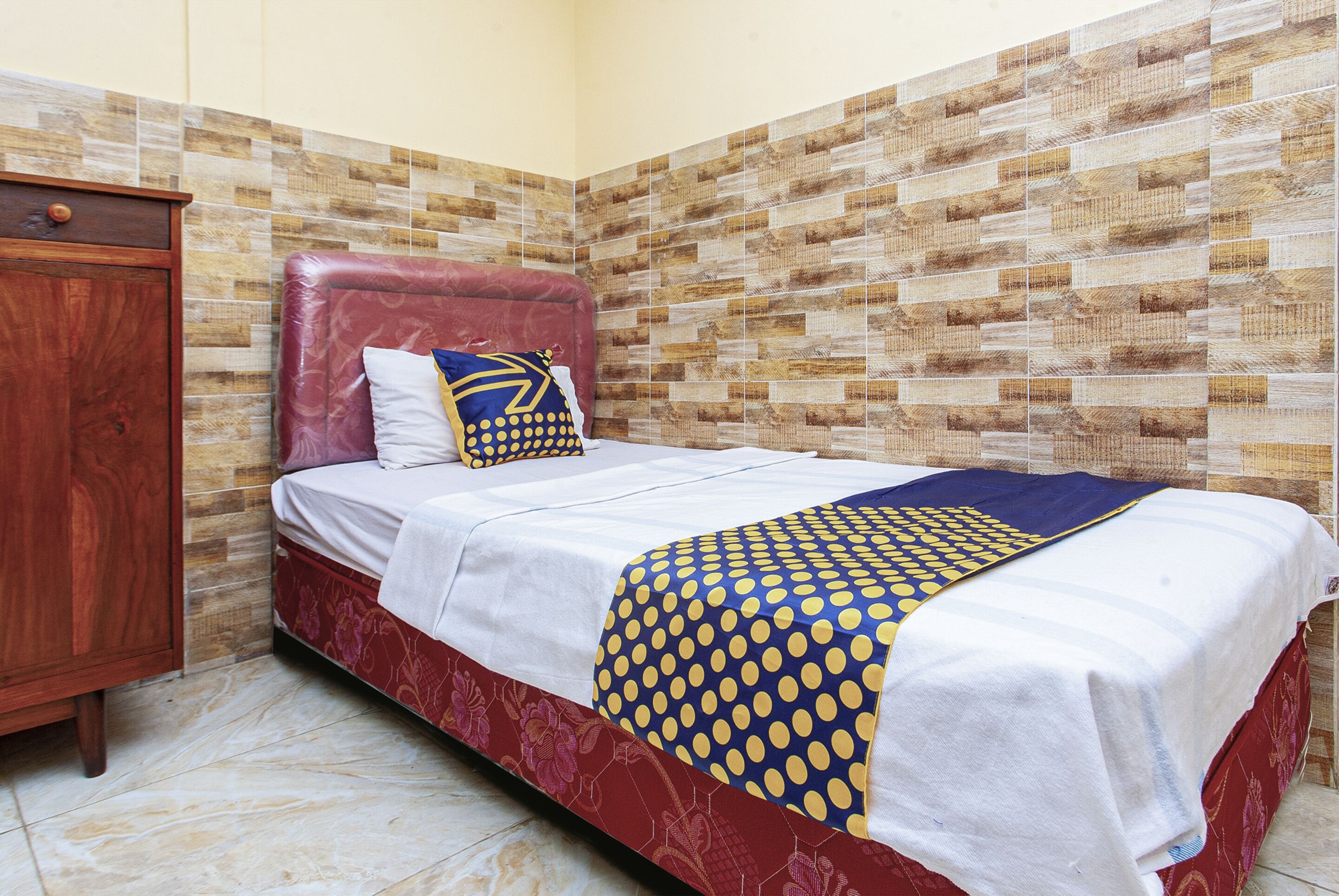 A bed with a patterned bedspread, a wooden cabinet, and a tiled wall.