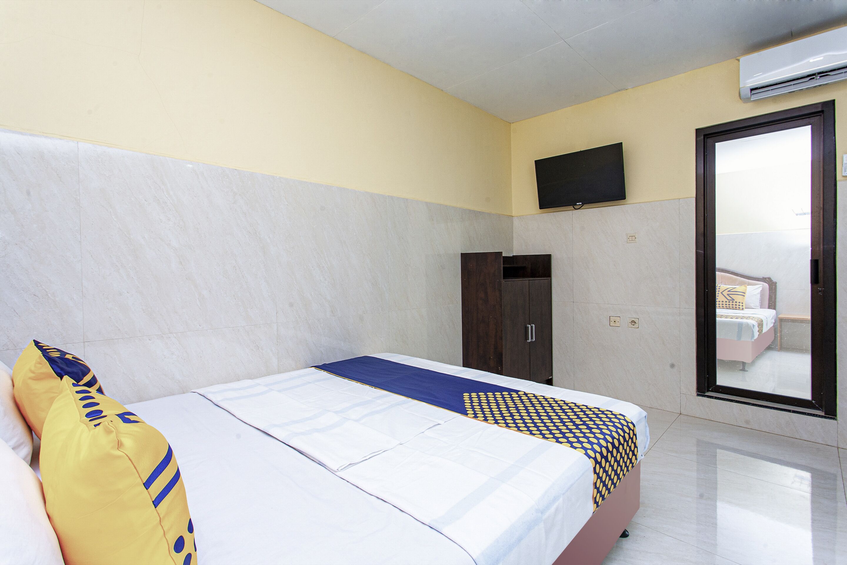 A hotel room with a bed, a wardrobe, a television mounted on the wall, and a sliding door leading to a balcony.