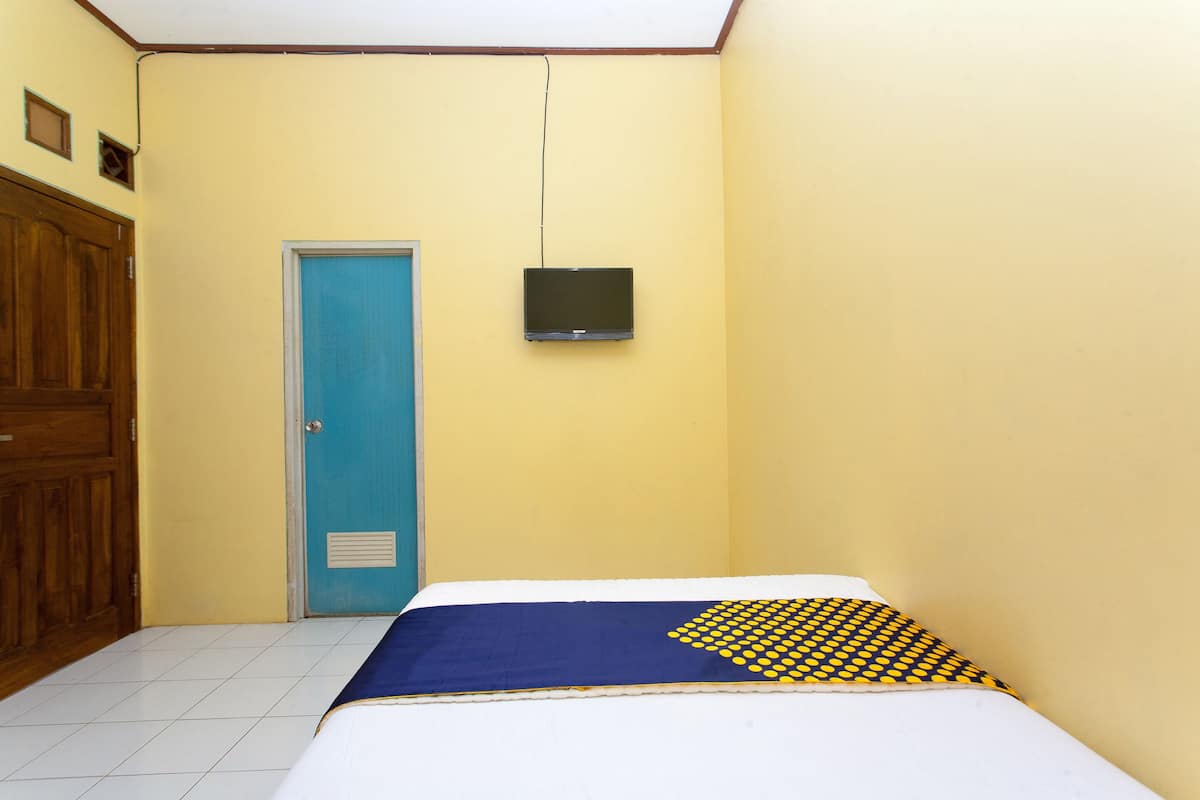 A room with a bed, a blue door, a television mounted on the wall, and a wooden wardrobe.