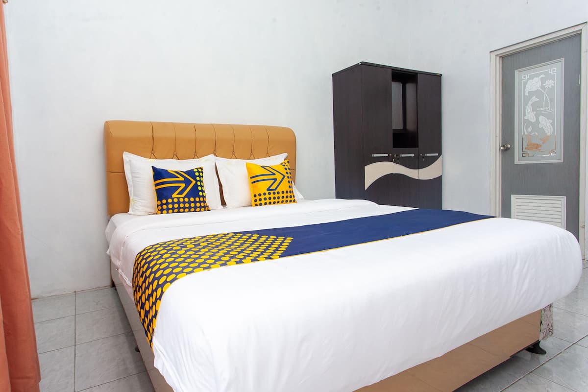 A bed with a white and yellow patterned bedspread, a brown upholstered headboard, and two pillows with yellow and blue patterns.