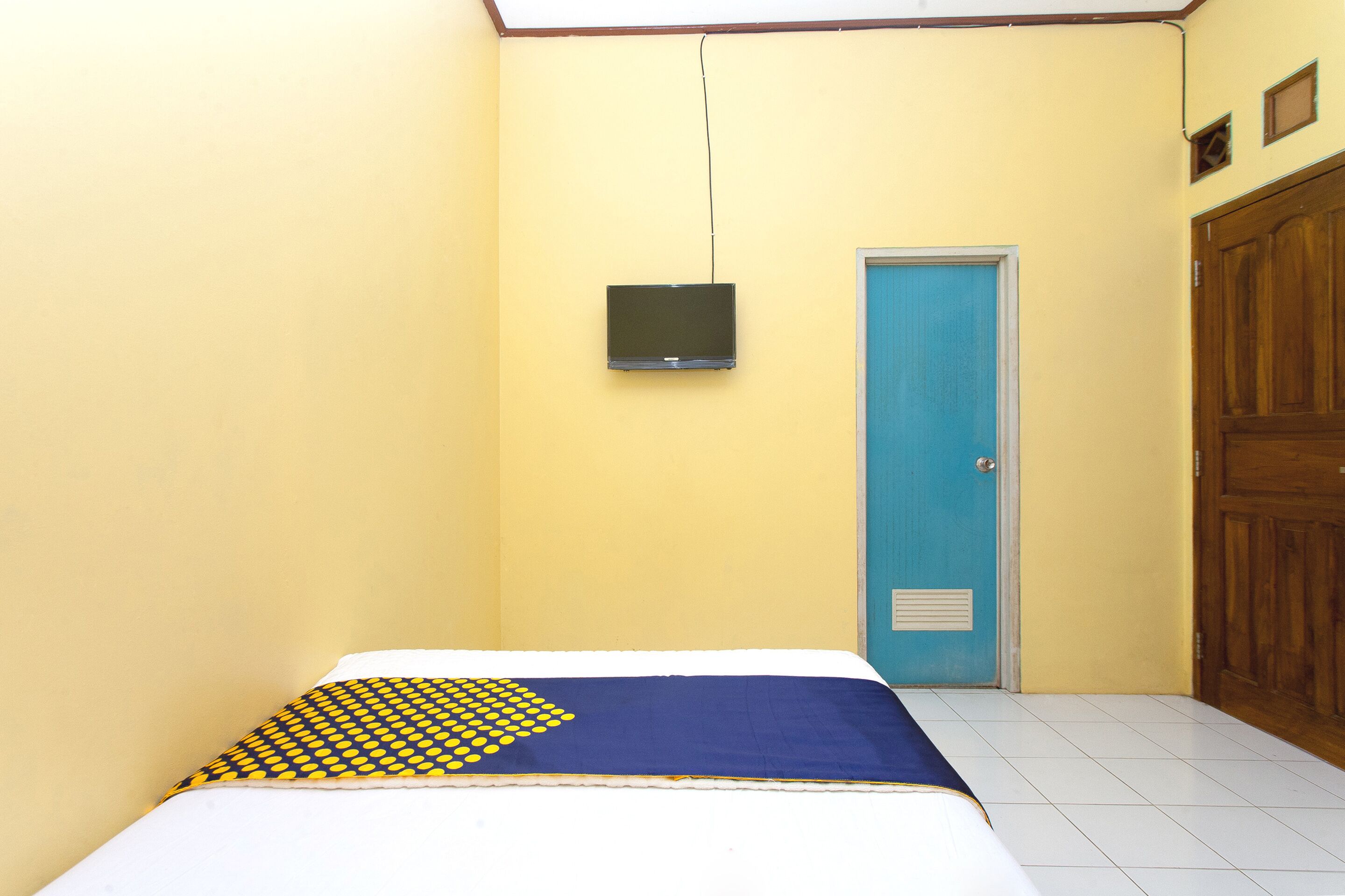 A room with a bed, a television mounted on the wall, a blue door, and a wooden wardrobe.
