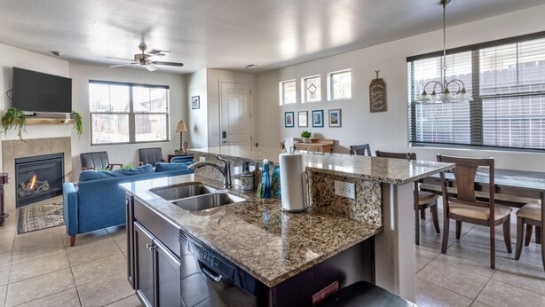 A modern kitchen with granite countertops, a built-in dishwasher, and a dining area with wooden chairs. - Lovely New Home in the North Woods (Flagstaff)