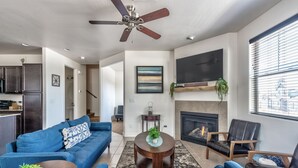 A modern living room with a blue sofa, a round coffee table, and a fireplace. - Lovely New Home in the North Woods (Flagstaff)