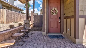 A covered patio with folding chairs, a red door with a wreath, and a wooden fence. - Lovely New Home in the North Woods (Flagstaff)