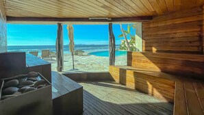 Un intérieur en bois avec une grande fenêtre donnant sur une plage et l’océan.