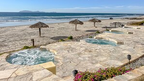 Un complexe hôtelier en bord de mer, doté de piscines en pierre, de parasols en chaume et offrant une vue sur l’océan.