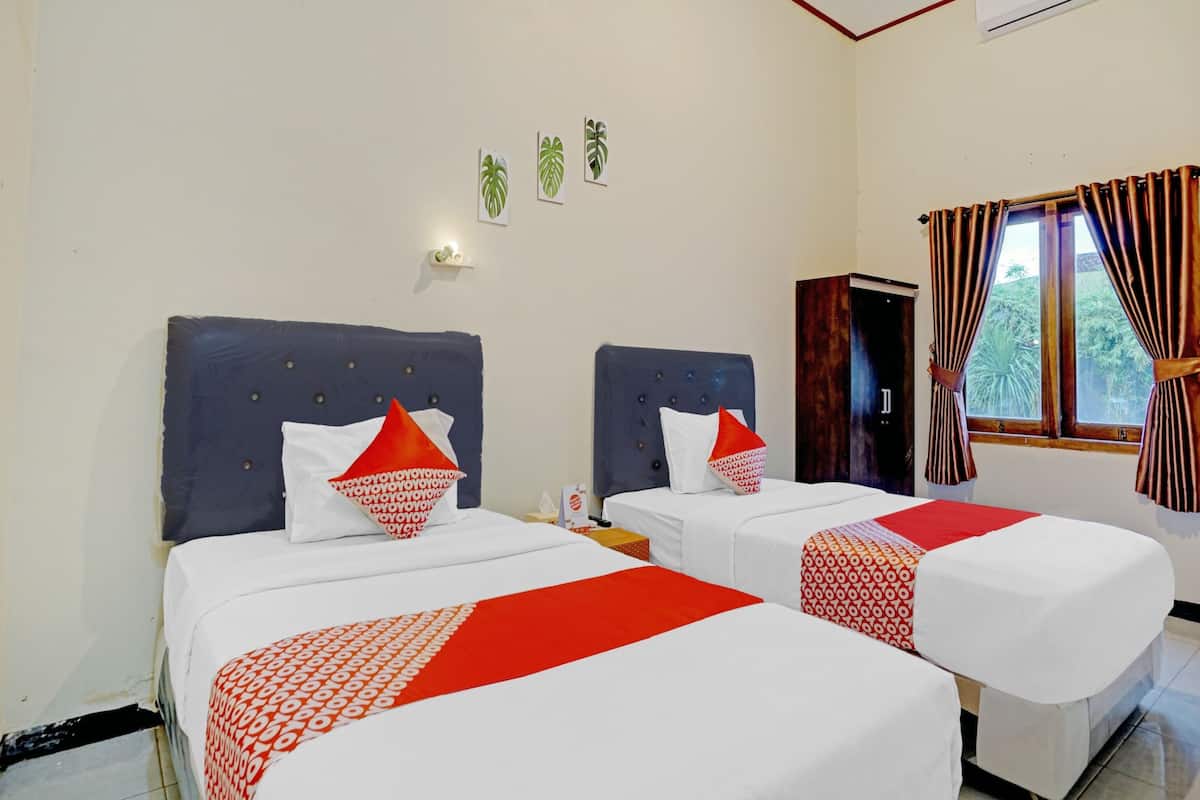A hotel room with two beds, each with a red and white patterned bedspread, and a window with curtains.