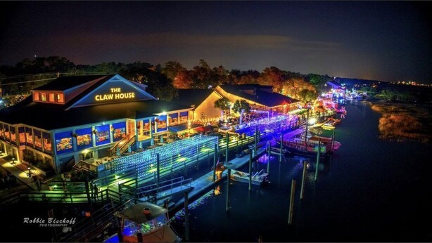 Een restaurant aan het water met een bord waarop staat 'The Claw House', met terras en een steiger met boten.