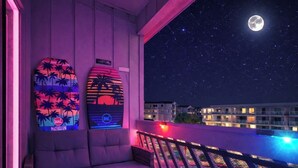 Een balkon met een bank en lounge stoelen, een zwembad met een nethek en een nachthemel met een zichtbare maan.