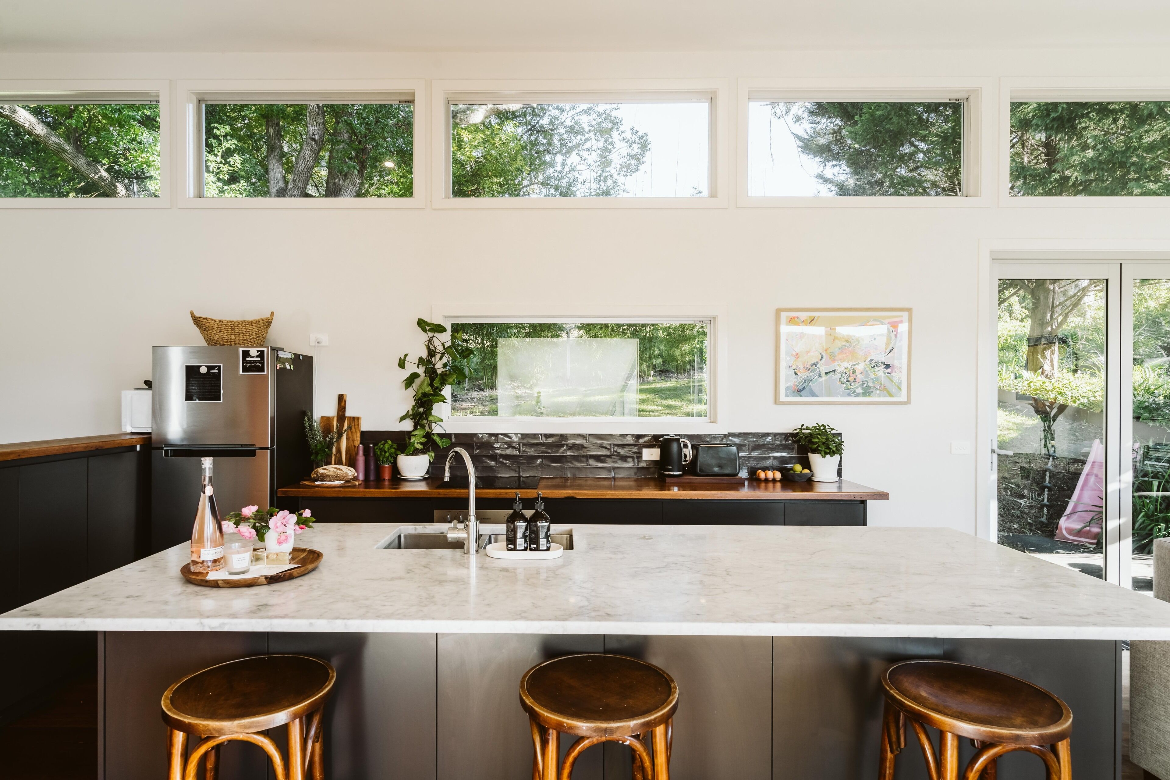 A modern kitchen with a large island, stainless steel appliances, and a view of the garden through large windows.