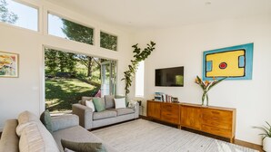 Un salon moderne avec une grande fenêtre, un canapé gris, un meuble en bois et un tableau accroché au mur.