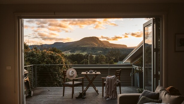 Un balcon avec une table et des chaises, un canapé et une vue sur une montagne au coucher du soleil.