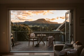 A balcony with a table and chairs, a sofa, and a view of a mountain at sunset. - The Tailor's Terrace Kangaroo valley. Modern spacious home with amazing views.  (Kangaroo Valley)