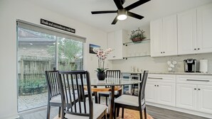 Una cucina moderna con mobili bianchi, un tavolo da pranzo in vetro e una ventola a soffitto.