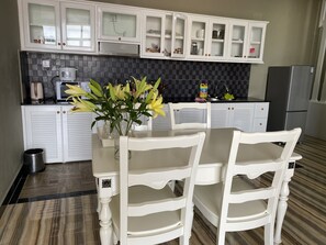 A kitchen with white cabinets, a black tiled backsplash, a stainless steel refrigerator, and a dining table with chairs.