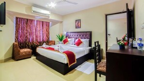 A hotel room with a bed, a desk, a chair, a television, and a ceiling fan. - Chirag Inn (Thiruvananthapuram)