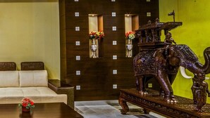 A lobby with a sofa, a coffee table with a flower, and an ornate elephant statue. - Chirag Inn (Thiruvananthapuram)