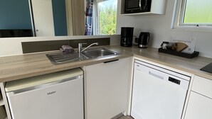 Una cocina compacta con armarios blancos, microondas integrado, cafetera y ventana que proporciona luz natural.