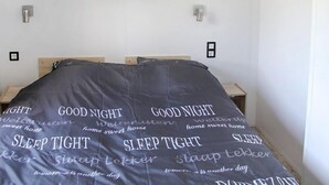 Un dormitorio con una cama cubierta por una colcha con frases motivacionales, dos mesitas de noche y una pared blanca con dos interruptores de luz.