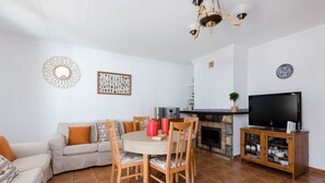 Una sala de estar con sofá, mesa de comedor, sillas, televisor y chimenea.