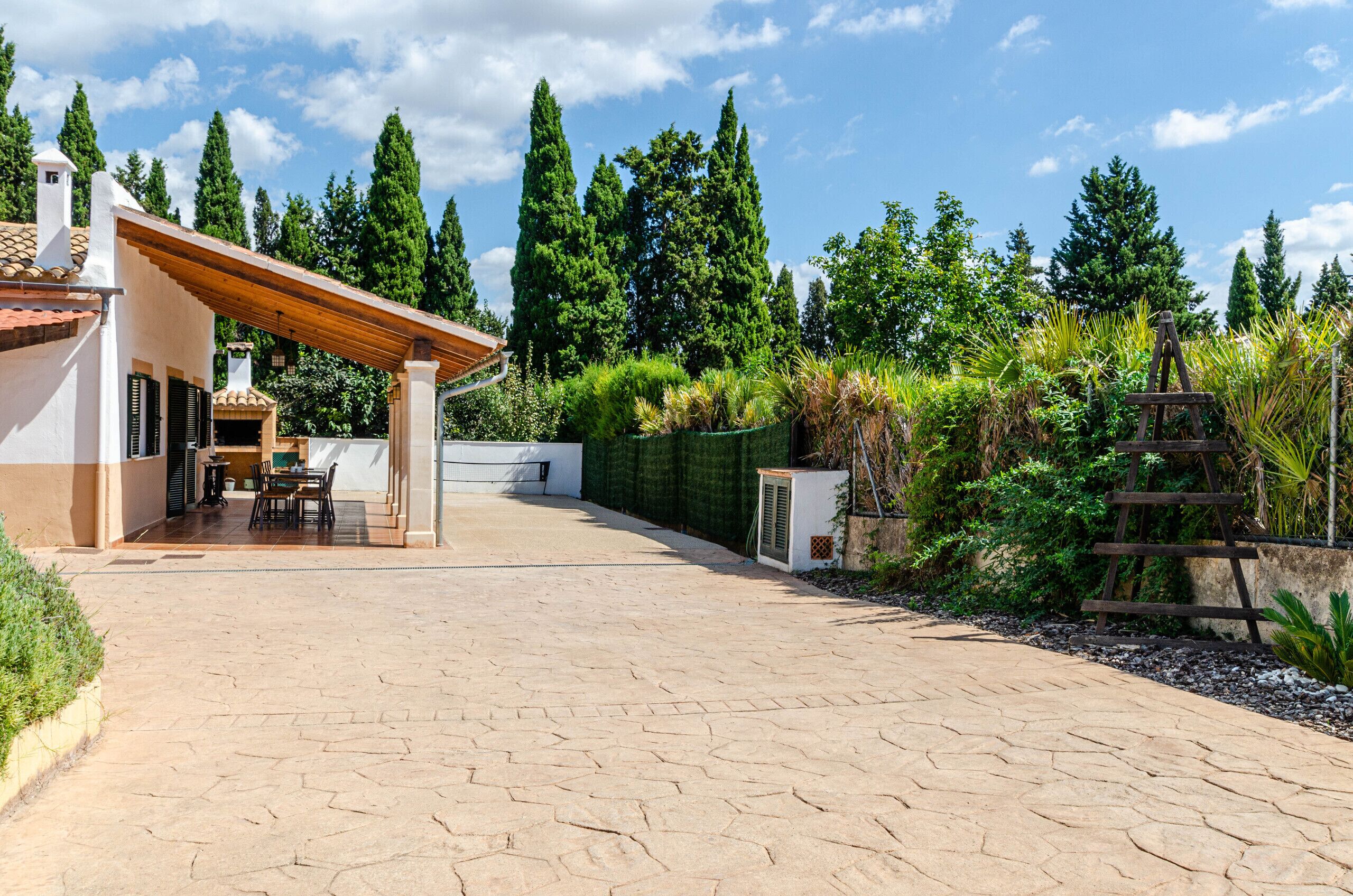 Un patio con una pérgola, comedor y vistas a árboles altos.