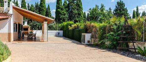 Un patio con una pérgola, comedor y vistas a árboles altos.
