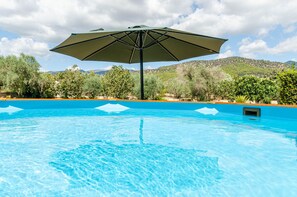 A swimming pool with a large umbrella, surrounded by trees and hills in the background. - YourHouse La Suerte (Binissalem)