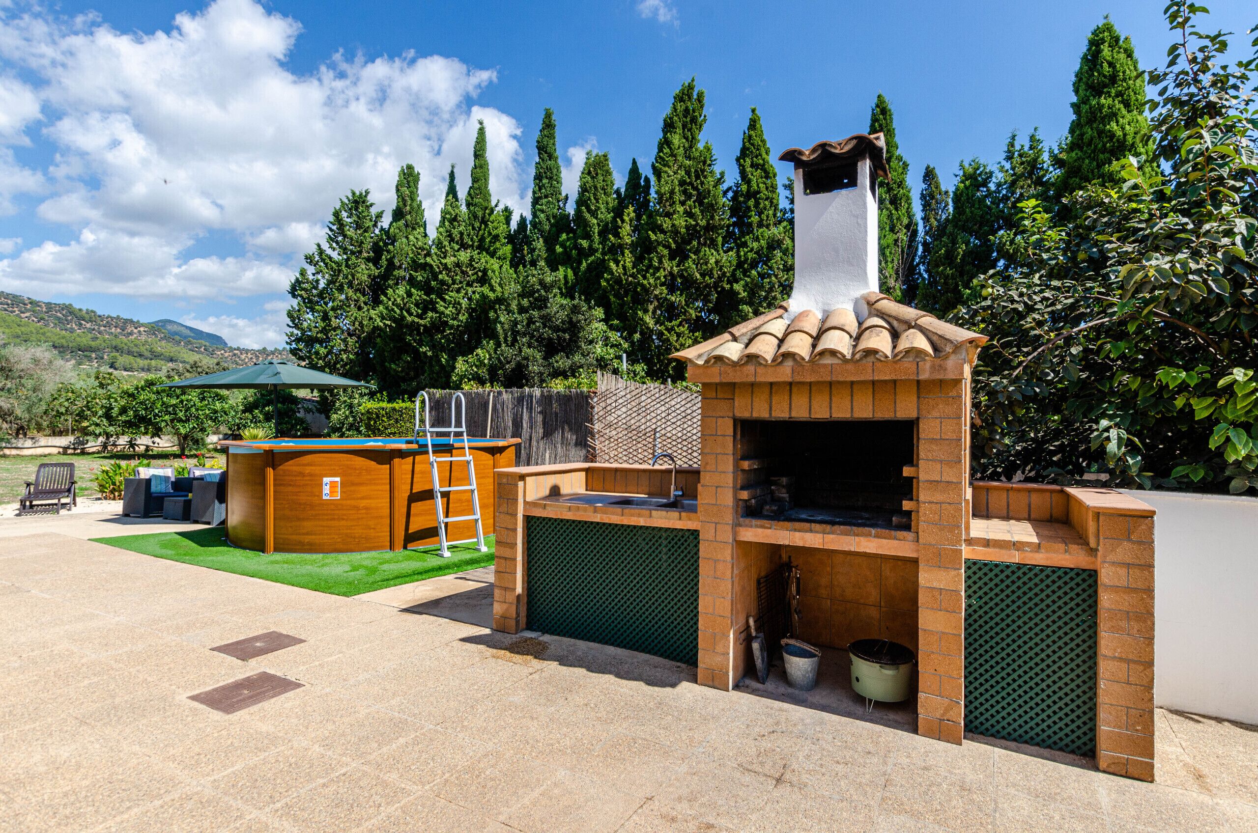 An outdoor kitchen area with a brick oven, a wooden structure, and a green umbrella.