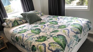 Een bed met een bloemenprint deken, donkere gordijnen en uitzicht op groen.