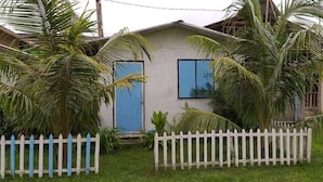 Una casa de un piso con fachada blanca, puerta azul y cerca de piquetes blancos.