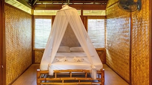 Una habitación con una cama bajo una dosel, paredes de madera y techo tejido.