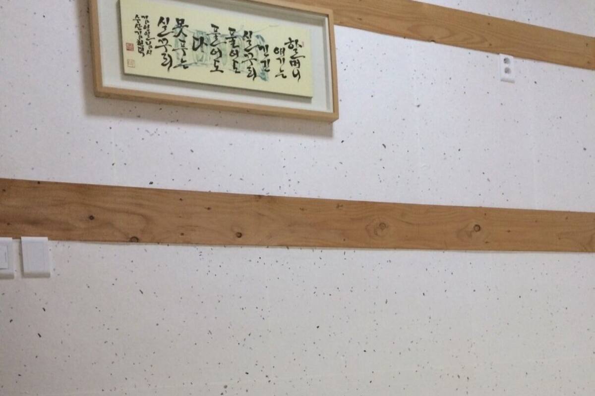 A bedroom with a bed, a framed calligraphy piece on the wall, and a small decorative item on the floor.