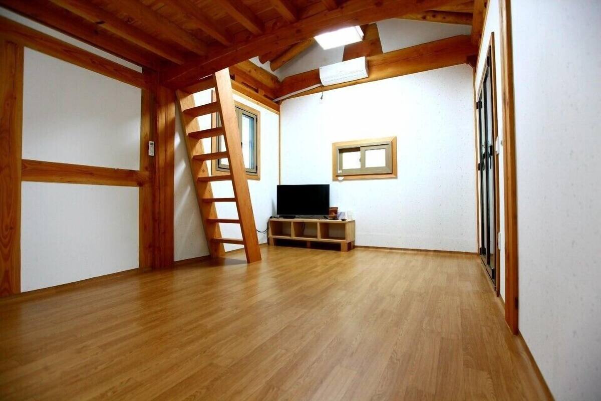 A room with wooden beams, a TV on a wooden stand, and a ladder against the wall.