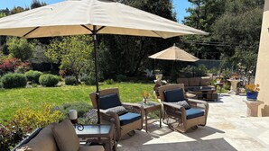Un patio al aire libre con muebles de mimbre, un paraguas grande y plantas en macetas.